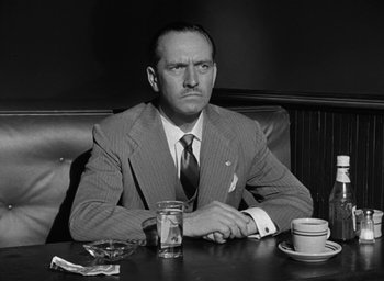 Movie still from “The Best Years of Our Lives” (1946), directed by William Wyler – A man sitting at a table with a cup of coffee in front of him; Medium shot, Low angle