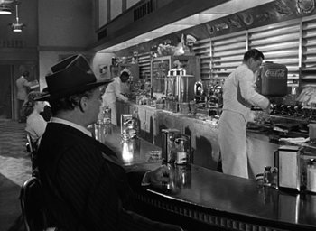 Movie still from “The Best Years of Our Lives” (1946), directed by William Wyler – A black and white photo of a man sitting at a counter; Medium shot, Over the shoulder angle