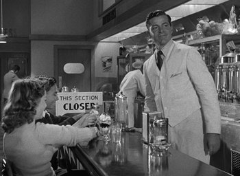 Movie still from “The Best Years of Our Lives” (1946), directed by William Wyler – A man standing at a counter in front of a woman; Medium shot, Over the shoulder angle