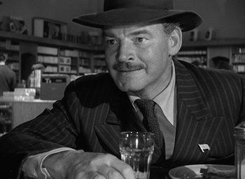 Movie still from “The Best Years of Our Lives” (1946), directed by William Wyler – A man in a suit and hat sitting at a table with a drink; Close Up shot, Over the shoulder angle