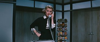 Movie still from “The Best of Everything” (1959), directed by Jean Negulesco – A woman talking on a phone while holding a suitcase; Medium shot, Low angle