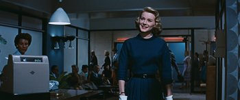 Movie still from “The Best of Everything” (1959), directed by Jean Negulesco – A woman in a blue dress standing in front of a group of people; Medium shot, Low angle