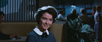 Movie still from “The Best of Everything” (1959), directed by Jean Negulesco – A woman with a hat sitting in a booth; Close Up shot, Over the shoulder angle