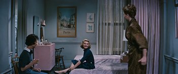 Movie still from “The Best of Everything” (1959), directed by Jean Negulesco – A woman sitting on top of a bed next to a dresser; Wide shot, Low angle