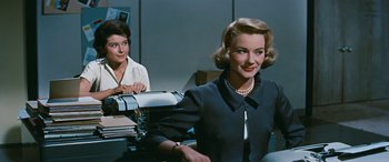 Movie still from “The Best of Everything” (1959), directed by Jean Negulesco – A woman in a black dress sitting in front of a desk; Medium shot, Low angle
