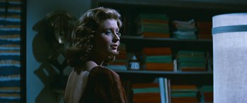 Movie still from “The Best of Everything” (1959), directed by Jean Negulesco – A woman in a brown dress in front of a book shelf; Close Up shot, Over the shoulder angle