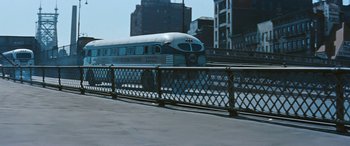 Movie still from “The Best of Everything” (1959), directed by Jean Negulesco – A bus driving down a street next to a bridge; Extreme Wide shot, High angle