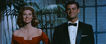 Movie still from “The Best of Everything” (1959), directed by Jean Negulesco – A man and a woman posing for a picture in front of palm trees; Medium shot, Low angle