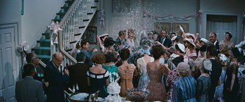 Movie still from “The Best of Everything” (1959), directed by Jean Negulesco – A group of people standing in a room with a cake; Wide shot, High angle