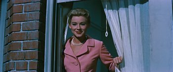 Movie still from “The Best of Everything” (1959), directed by Jean Negulesco – A woman in a pink suit standing in front of a window; Medium shot, Low angle
