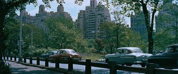 Movie still from “The Best of Everything” (1959), directed by Jean Negulesco – Cars are parked on the side of the road near a bridge; Extreme Wide shot, High angle