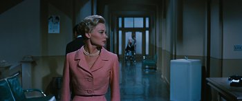 Movie still from “The Best of Everything” (1959), directed by Jean Negulesco – A woman in a pink dress and pearls in a hallway; Medium shot, Low angle