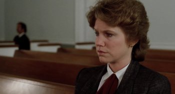 Movie still from “The Big Chill” (1983), directed by Lawrence Kasdan – A woman in a suit and tie sitting in a courtroom; Close Up shot, Over the shoulder angle