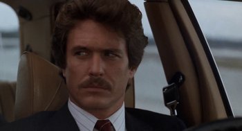 Movie still from “The Big Chill” (1983), directed by Lawrence Kasdan – A man in a suit and tie in a car; Close Up shot, Low angle