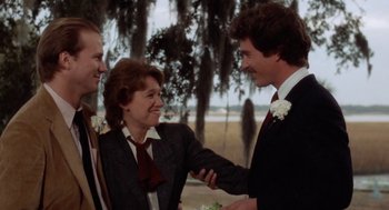 Movie still from “The Big Chill” (1983), directed by Lawrence Kasdan – Two men and a woman shaking hands in front of trees; Medium shot, Over the shoulder angle