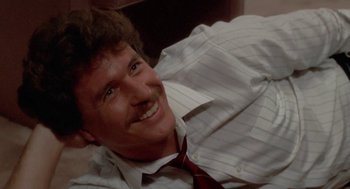 Movie still from “The Big Chill” (1983), directed by Lawrence Kasdan – A man in a striped dress shirt and a red neck tie smiling; Close Up shot, High angle