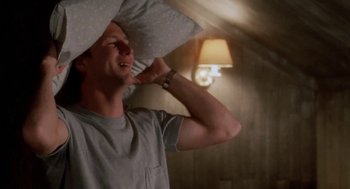 Movie still from “The Big Chill” (1983), directed by Lawrence Kasdan – A man holding a pillow over his head while standing in a room; Medium shot, Low angle