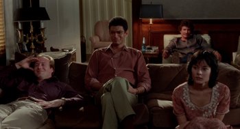 Movie still from “The Big Chill” (1983), directed by Lawrence Kasdan – A man sitting on top of a couch next to two other people; Wide shot, High angle