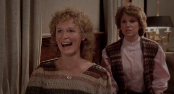 Movie still from “The Big Chill” (1983), directed by Lawrence Kasdan – Two women are smiling for the camera in front of a piano; Medium shot, Over the shoulder angle