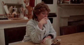 Movie still from “The Big Chill” (1983), directed by Lawrence Kasdan – A woman sitting at a table with a cup of coffee in front of her mouth; Medium shot, Low angle