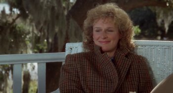 Movie still from “The Big Chill” (1983), directed by Lawrence Kasdan – A person sitting on a chair near a tree; Medium shot, Over the shoulder angle