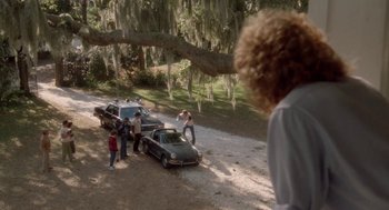 Movie still from “The Big Chill” (1983), directed by Lawrence Kasdan – A group of people standing next to a couple of parked cars; Wide shot, Over the shoulder angle