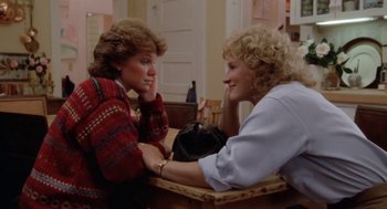 Movie still from “The Big Chill” (1983), directed by Lawrence Kasdan – Two women sitting at a table talking to each other; Medium shot, High angle