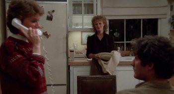 Movie still from “The Big Chill” (1983), directed by Lawrence Kasdan – A woman holding a plate in a kitchen; Medium shot, Over the shoulder angle