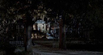 Movie still from “The Big Chill” (1983), directed by Lawrence Kasdan – A cemetery with a wrought - iron gate in front of a house at night; Extreme Wide shot, High angle