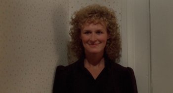 Movie still from “The Big Chill” (1983), directed by Lawrence Kasdan – A woman with curly blonde hair smiling for the camera; Close Up shot, Over the shoulder angle