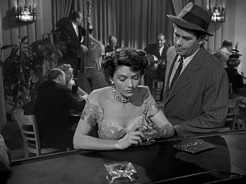 Movie still from “The Big Heat” (1953), directed by Fritz Lang – A man and a woman sitting at a table in front of other people; Medium shot, High angle