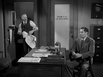Movie still from “The Big Heat” (1953), directed by Fritz Lang – Two men in suits are sitting at a desk in a room; Medium shot, Low angle