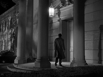 Movie still from “The Big Heat” (1953), directed by Fritz Lang – A man wearing a hat and a long coat walking in front of a building at night; Wide shot, Low angle