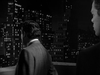 Movie still from “The Big Heat” (1953), directed by Fritz Lang – A black and white photo of a man standing in front of a city; Medium shot, Over the shoulder angle