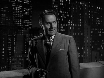 Movie still from “The Big Heat” (1953), directed by Fritz Lang – A man wearing a suit and tie standing on a balcony; Medium shot, Low angle