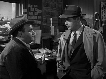 Movie still from “The Big Heat” (1953), directed by Fritz Lang – Two men in suits and hats talking to each other in an office; Medium shot, Over the shoulder angle