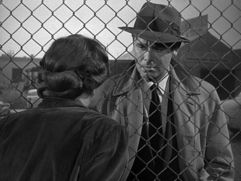 Movie still from “The Big Heat” (1953), directed by Fritz Lang – A man and a woman are standing in front of a chain link fence; Medium shot, Over the shoulder angle