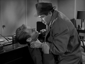 Movie still from “The Big Heat” (1953), directed by Fritz Lang – A man in a hat and a man in a trench coat and a hat is combing another man's hair; Medium shot, Over the shoulder angle