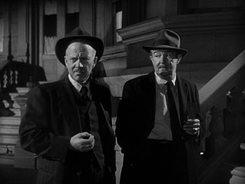 Movie still from “The Big Heat” (1953), directed by Fritz Lang – Two older men standing next to each other holding drinks; Medium shot, Low angle