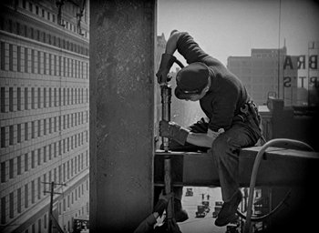 Movie still from “The Big Parade” (1925), directed by King Vidor – A man working on a metal structure on a building; Wide shot, Low angle
