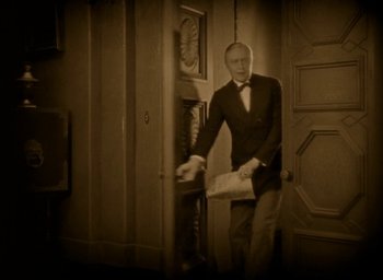 Movie still from “The Big Parade” (1925), directed by King Vidor – A man in a suit and tie standing in front of an open door; Medium shot, High angle