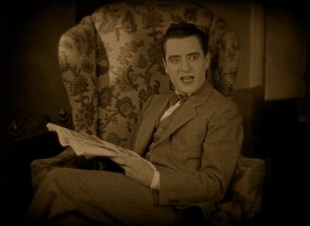 Movie still from “The Big Parade” (1925), directed by King Vidor – A man sitting in a chair reading a newspaper; Medium shot, High angle