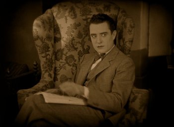 Movie still from “The Big Parade” (1925), directed by King Vidor – A man sitting in an arm chair holding a book; Medium shot, High angle