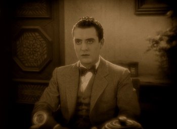 Movie still from “The Big Parade” (1925), directed by King Vidor – A man in a suit and bow tie sitting at a table; Close Up shot, High angle