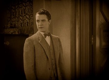 Movie still from “The Big Parade” (1925), directed by King Vidor – A man in a suit and bow tie standing next to a wall; Medium shot, High angle