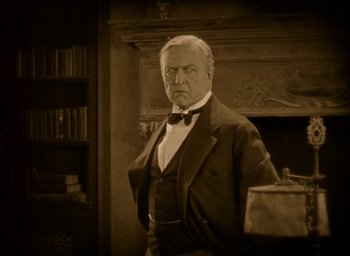 Movie still from “The Big Parade” (1925), directed by King Vidor – An older man in a suit and bow tie in front of a fireplace; Medium shot, Low angle