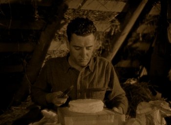 Movie still from “The Big Parade” (1925), directed by King Vidor – A man sitting in front of a cake with a knife in his hand; Medium shot, High angle
