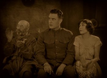 Movie still from “The Big Parade” (1925), directed by King Vidor – An old photo of a man and two women sitting on a bench; Medium shot, High angle