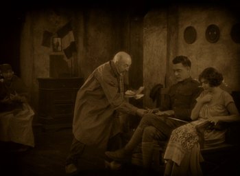 Movie still from “The Big Parade” (1925), directed by King Vidor – An old man is giving a woman a pair of shoes; Medium shot, High angle