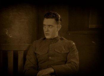 Movie still from “The Big Parade” (1925), directed by King Vidor – A man wearing a uniform sitting in a chair; Medium shot, High angle